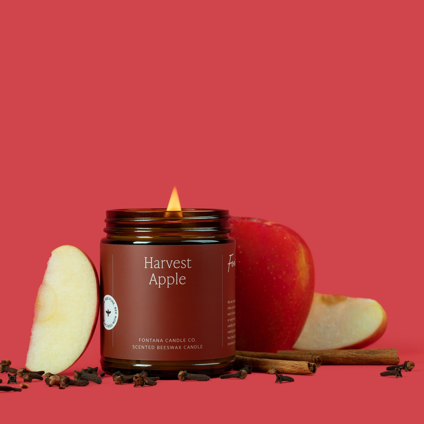 Lit Harvest Apple jar candle with apples and cinnamon on a red background.
