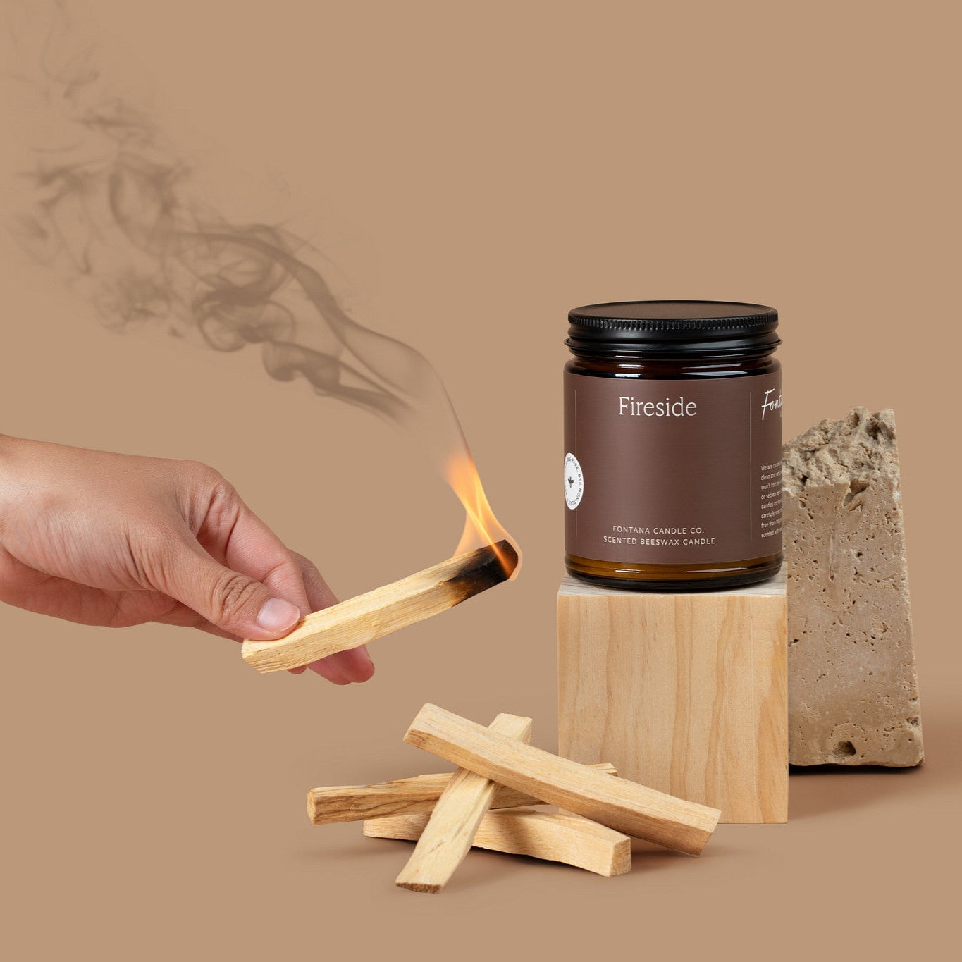 Amber glass jar candle labeled 'Fireside' with lit Palo Santo sticks on a beige background