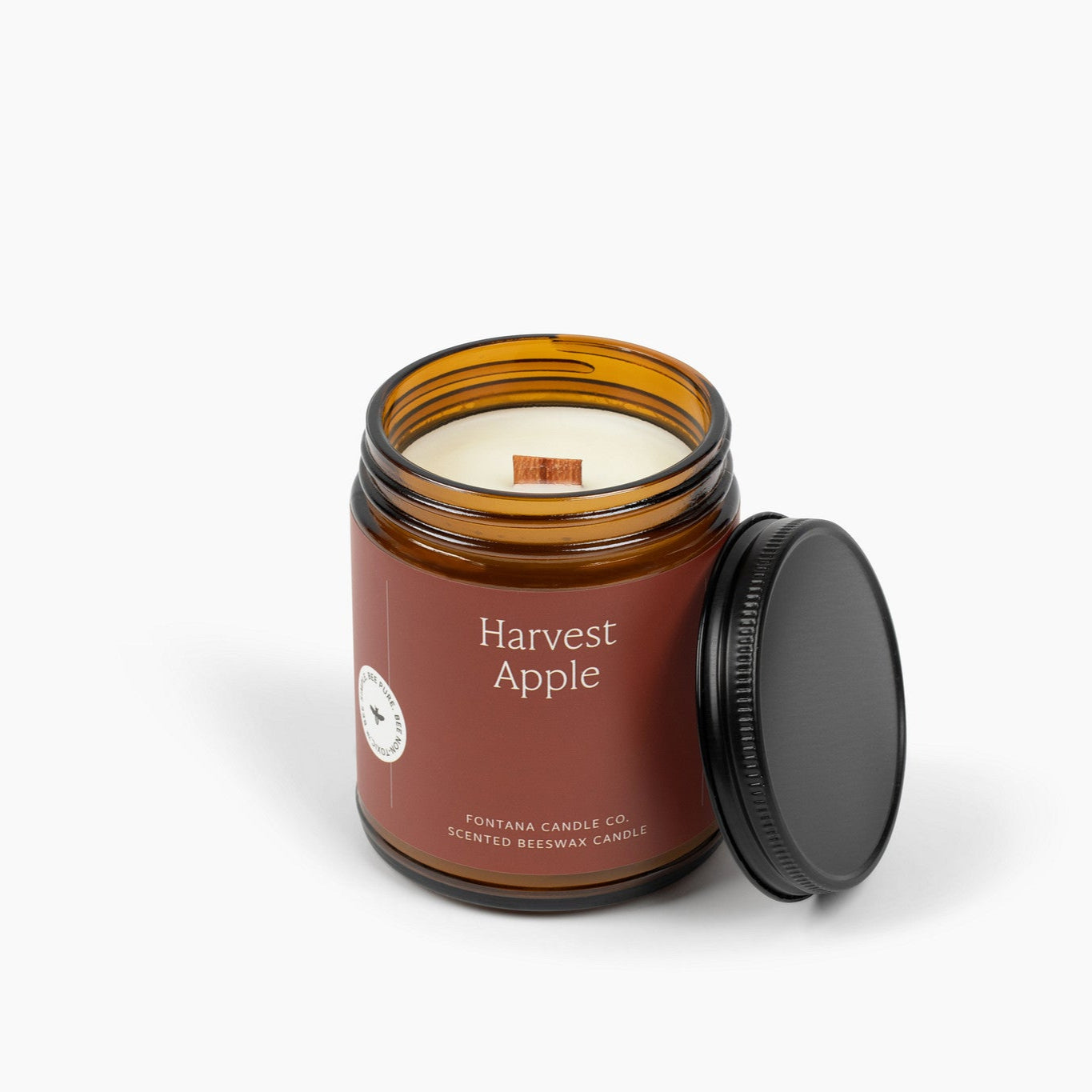 Unlit amber glass jar candle with a wooden wick and deep red label with the scent Harvest Apple.