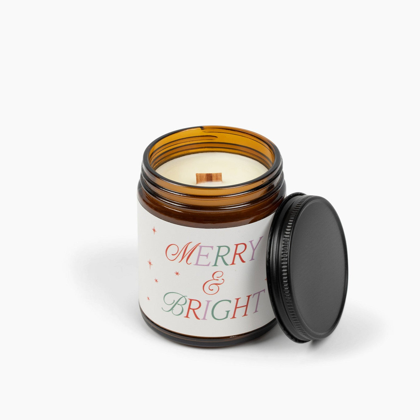 Unlit amber glass jar candle with a wooden wick and a cream colored label with the festive holiday text that says: Merry & Bright.