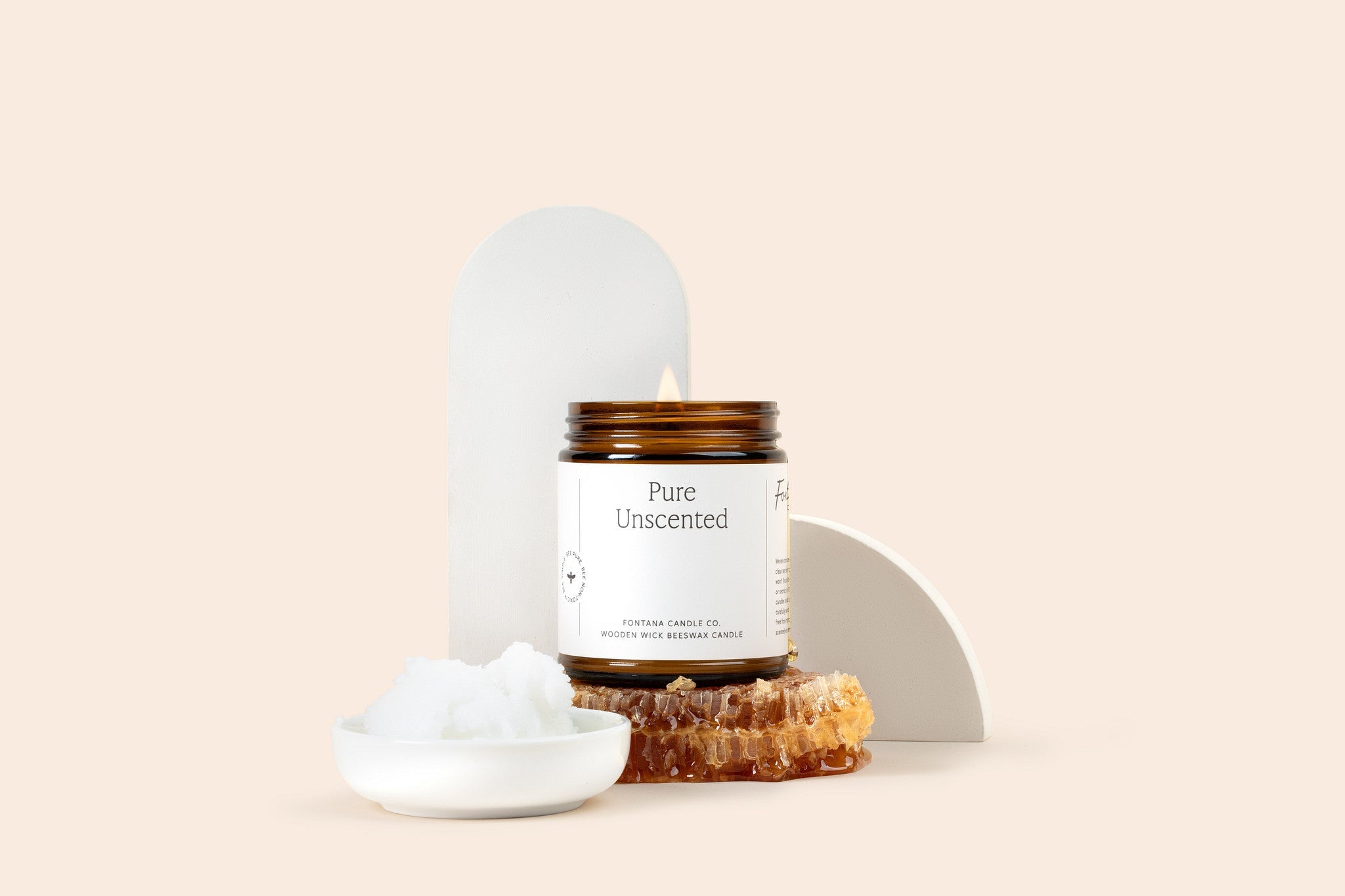 Lit amber glass jar candle with a white label, sitting on top of honey comb, in front of a beige background.