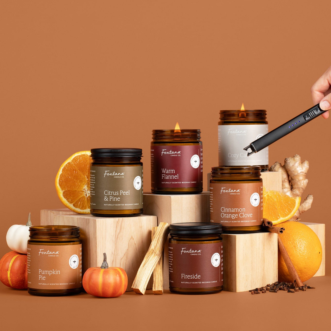 Collection of candles with pumpkins, oranges, and cinnamon sticks on a brown background