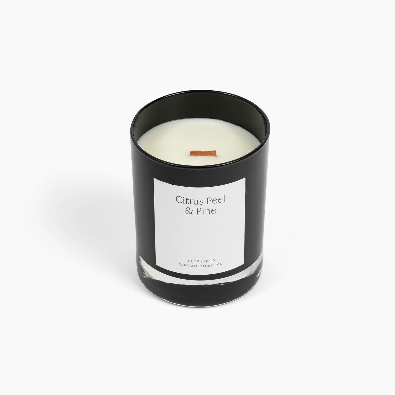 A black glass Noir candle with a white label reading 'Citrus Peel &amp; Pine' and a wooden wick, photographed on a clean white background.