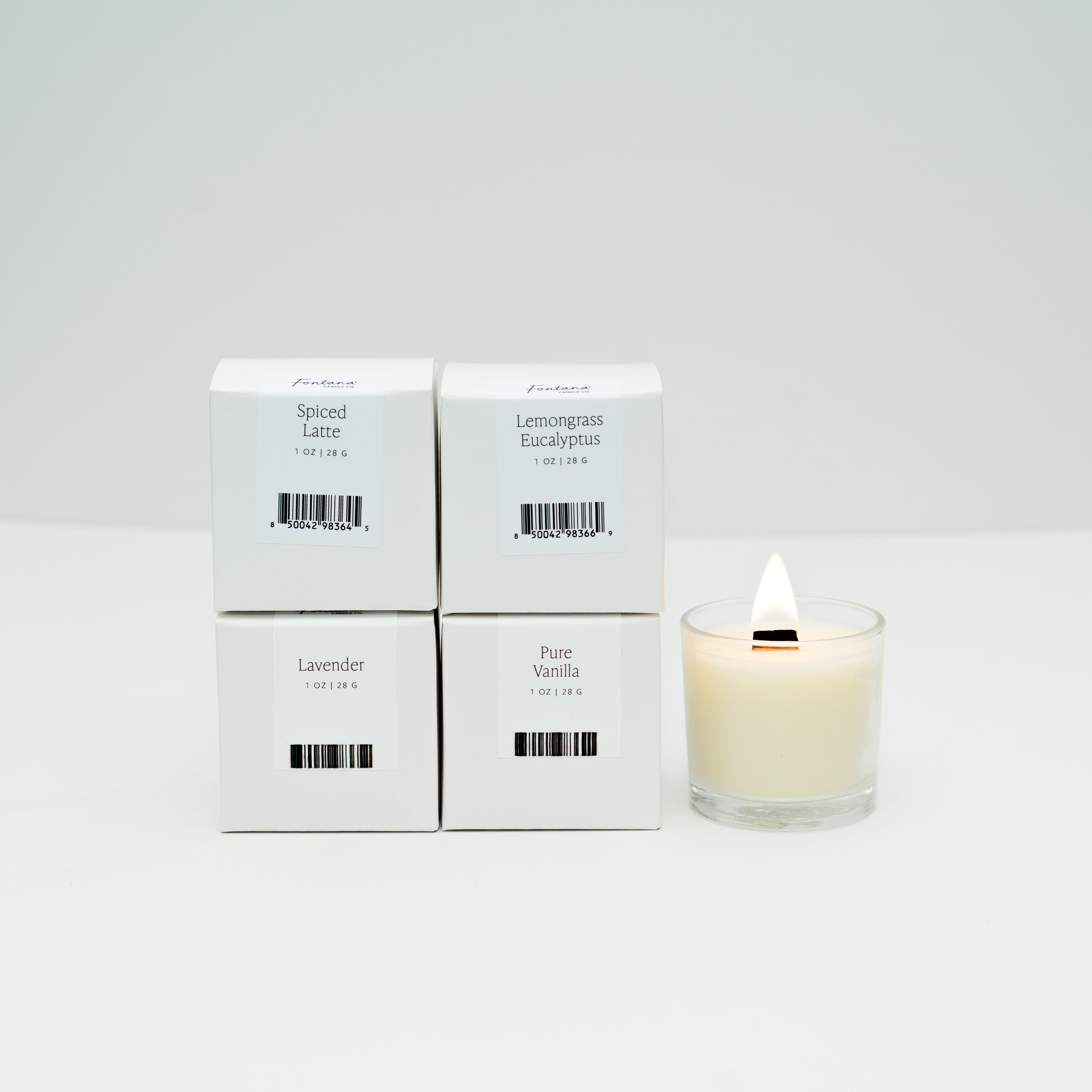 Four boxes of Mini candles next to one lit mini glass votive candle, on a white background.