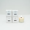 Four boxes of Mini candles next to one lit mini glass votive candle, on a white background.