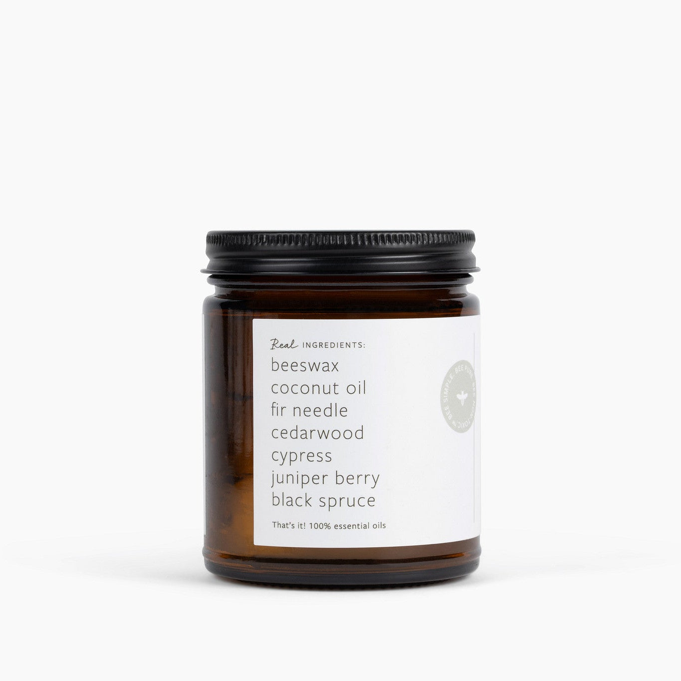 An amber glass jar candle with a black metal lid and a white label, photographed on a clean white background. The label reads 'Real Ingredients' and lists ingredients including beeswax, coconut oil, fir needle, cedarwood, cypress, juniper berry, and black spruce.