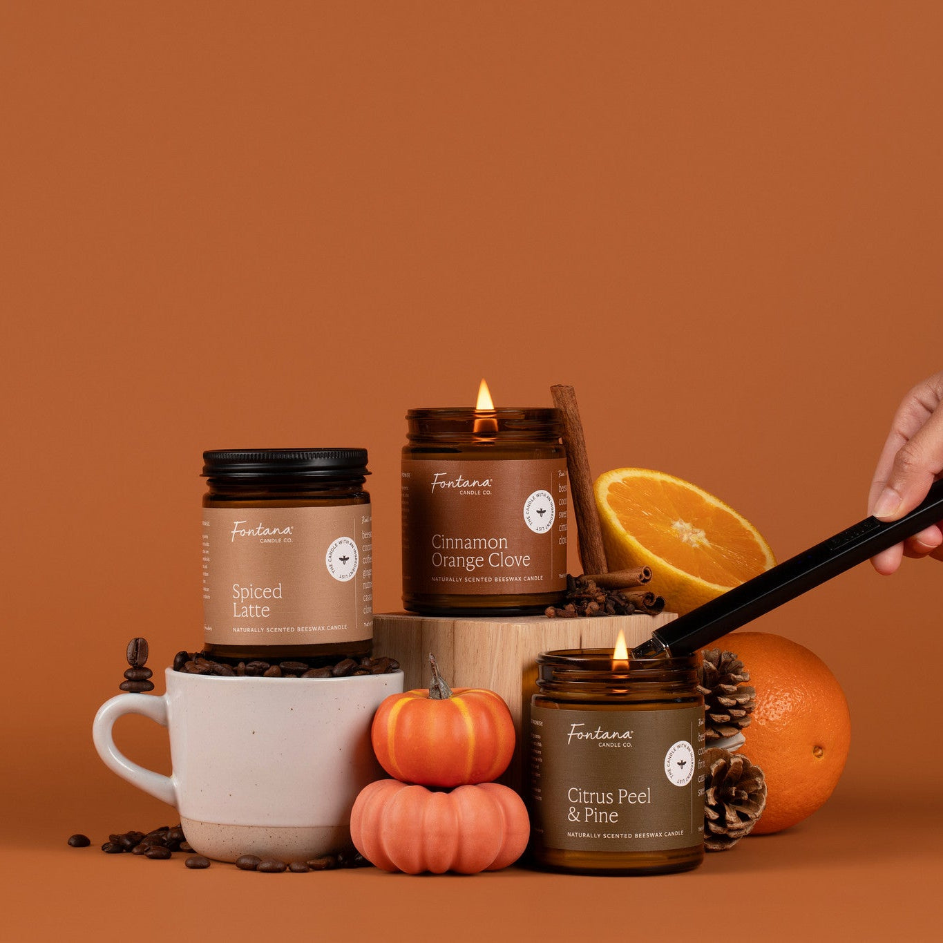 Collection of candles, coffee items, oranges and pinecones on an orange background