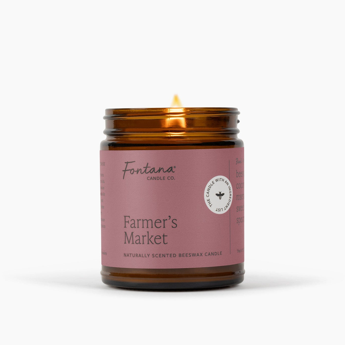 Lit amber glass jar candle with 'Farmer's Market' label on a white background.