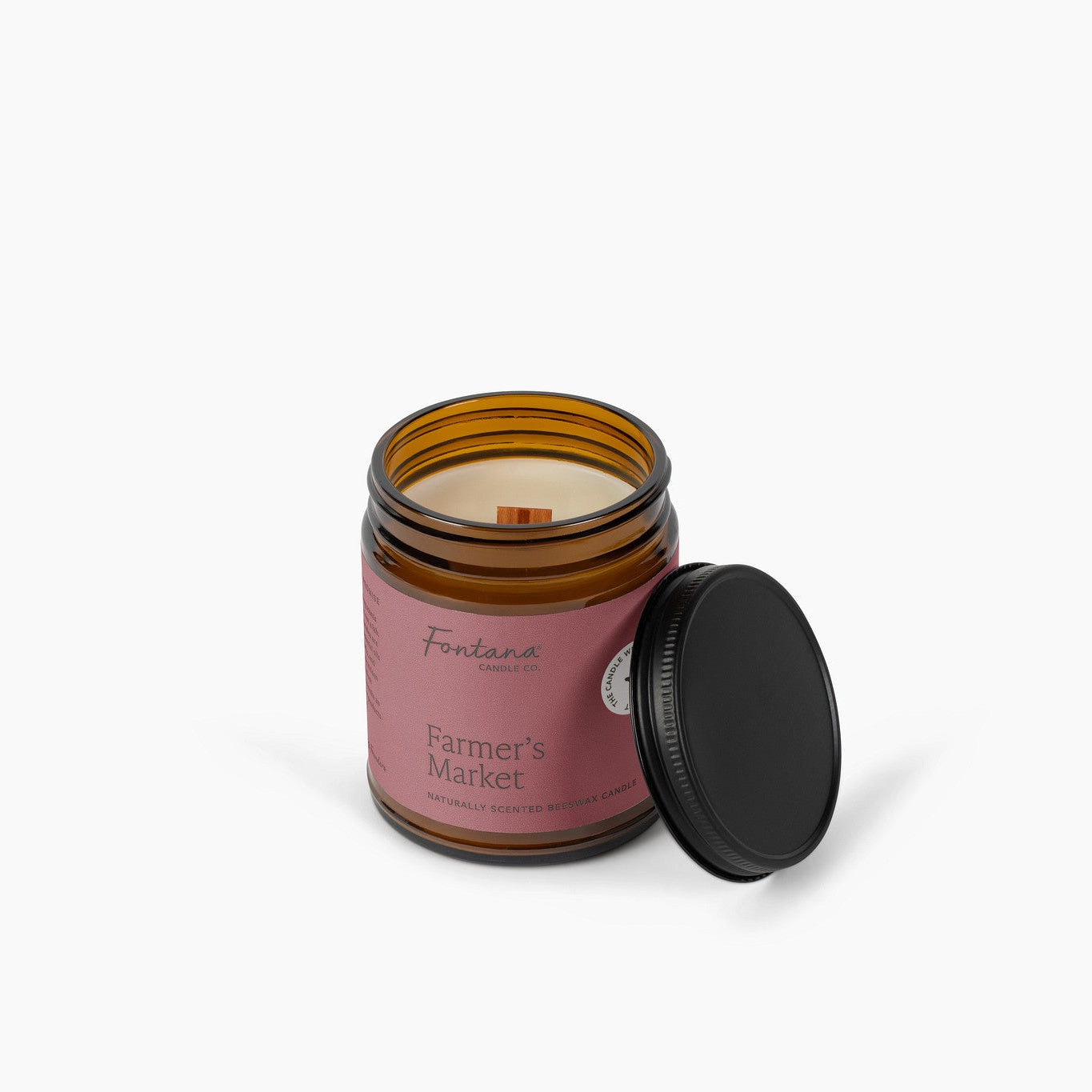 amber glass jar candle, unlit with the wooden wick visible, red/pink label that says farmer's market on a white background