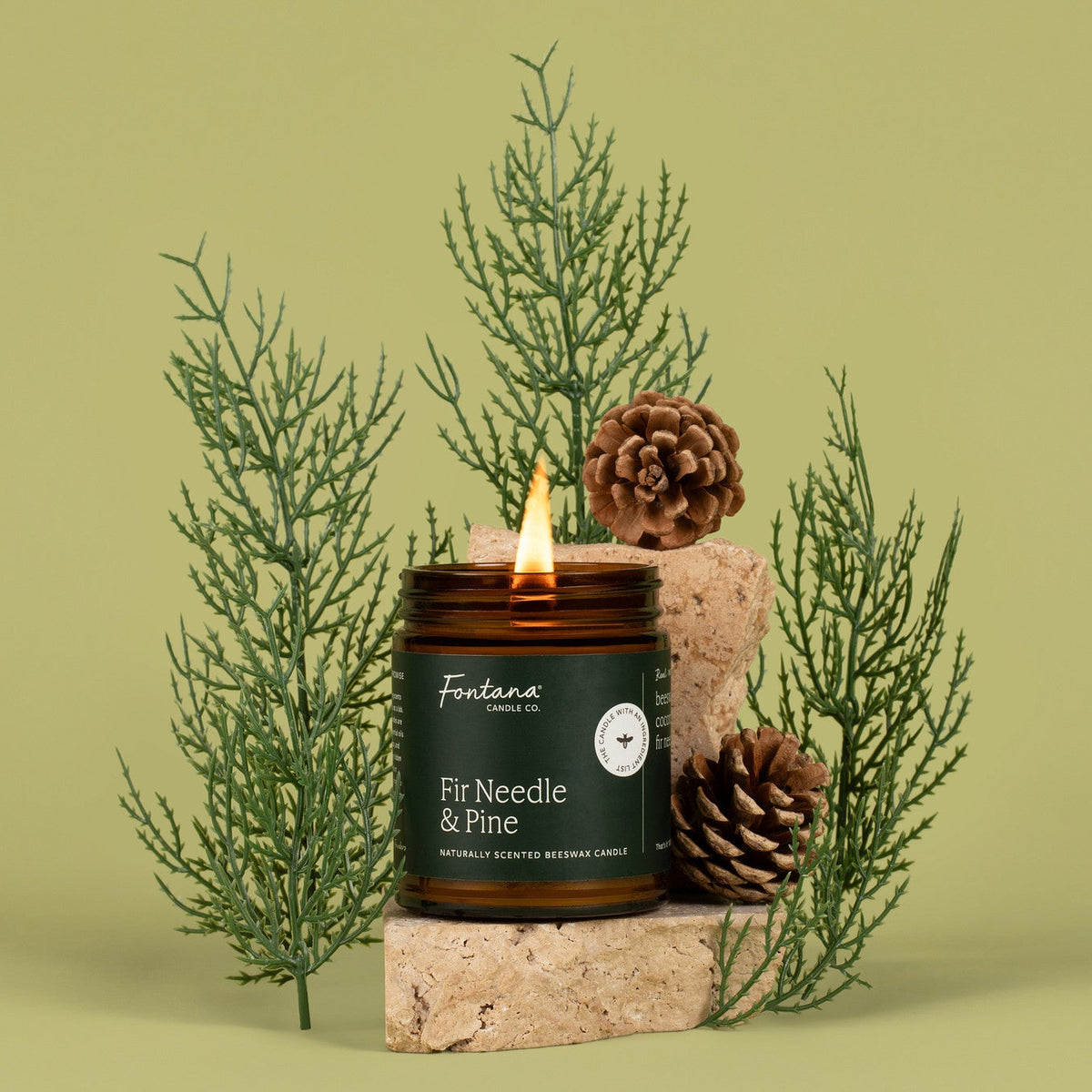 Candle labeled 'Fir Needle &amp; Pine' with decorative elements on a green background