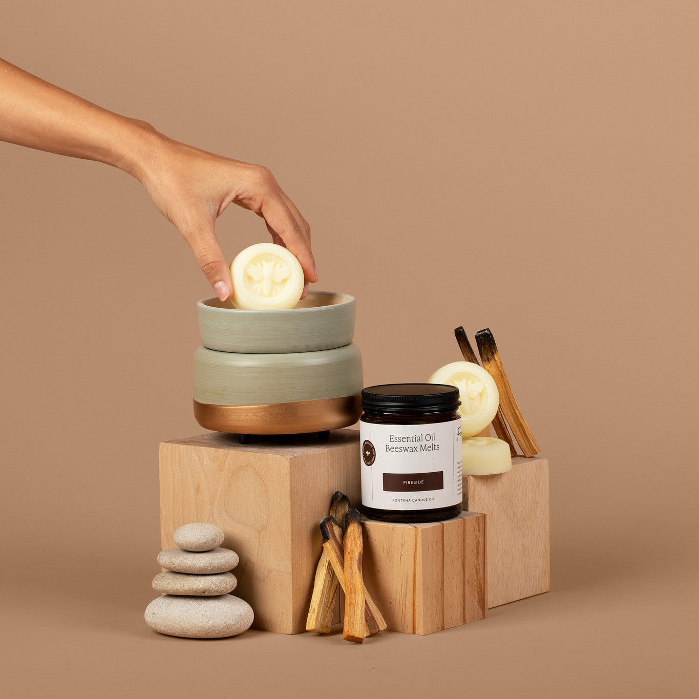 Hand reaching for a wax melt on a wooden block with a jar on a brown background