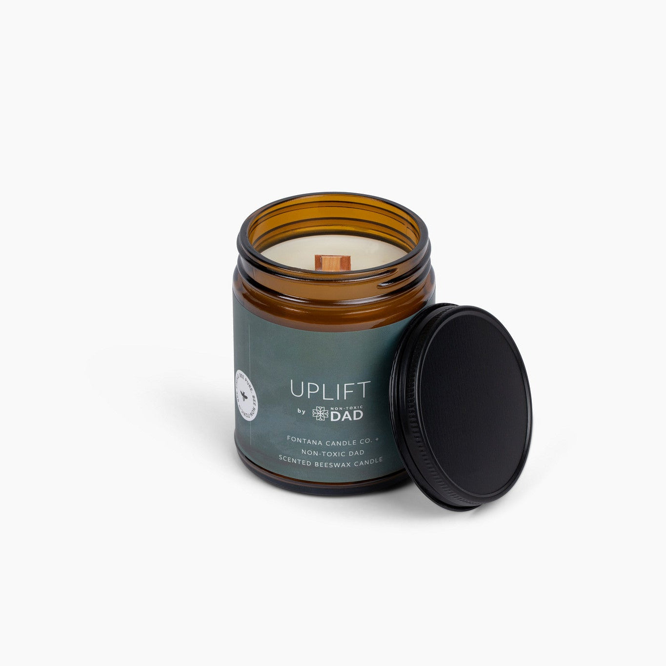 Amber glass jar candle with a wooden wick and a green label, on a white background.