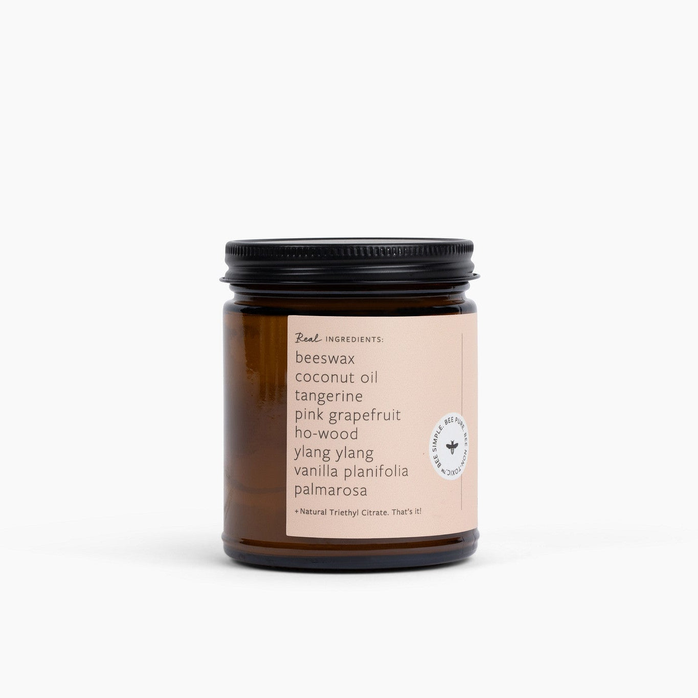 Side view of an amber glass candle jar with a peach colored label on a white background.