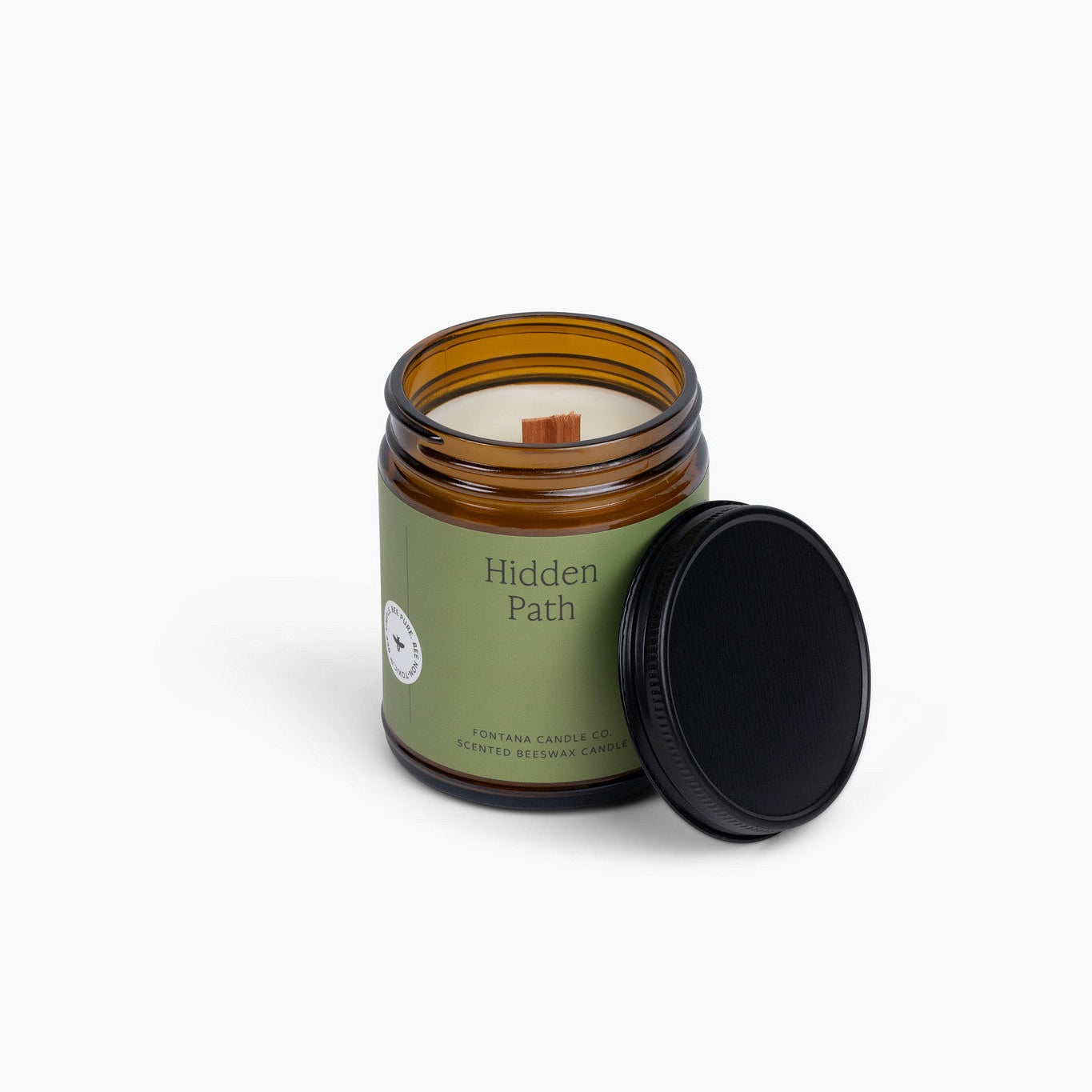 Amber glass jar candle with a wooden wick and a green label, on a white background.