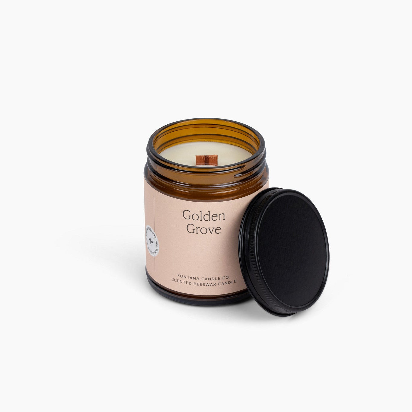 Candle in an amber glass jar labeled 'Golden Grove' with a peach colored label, on a white background