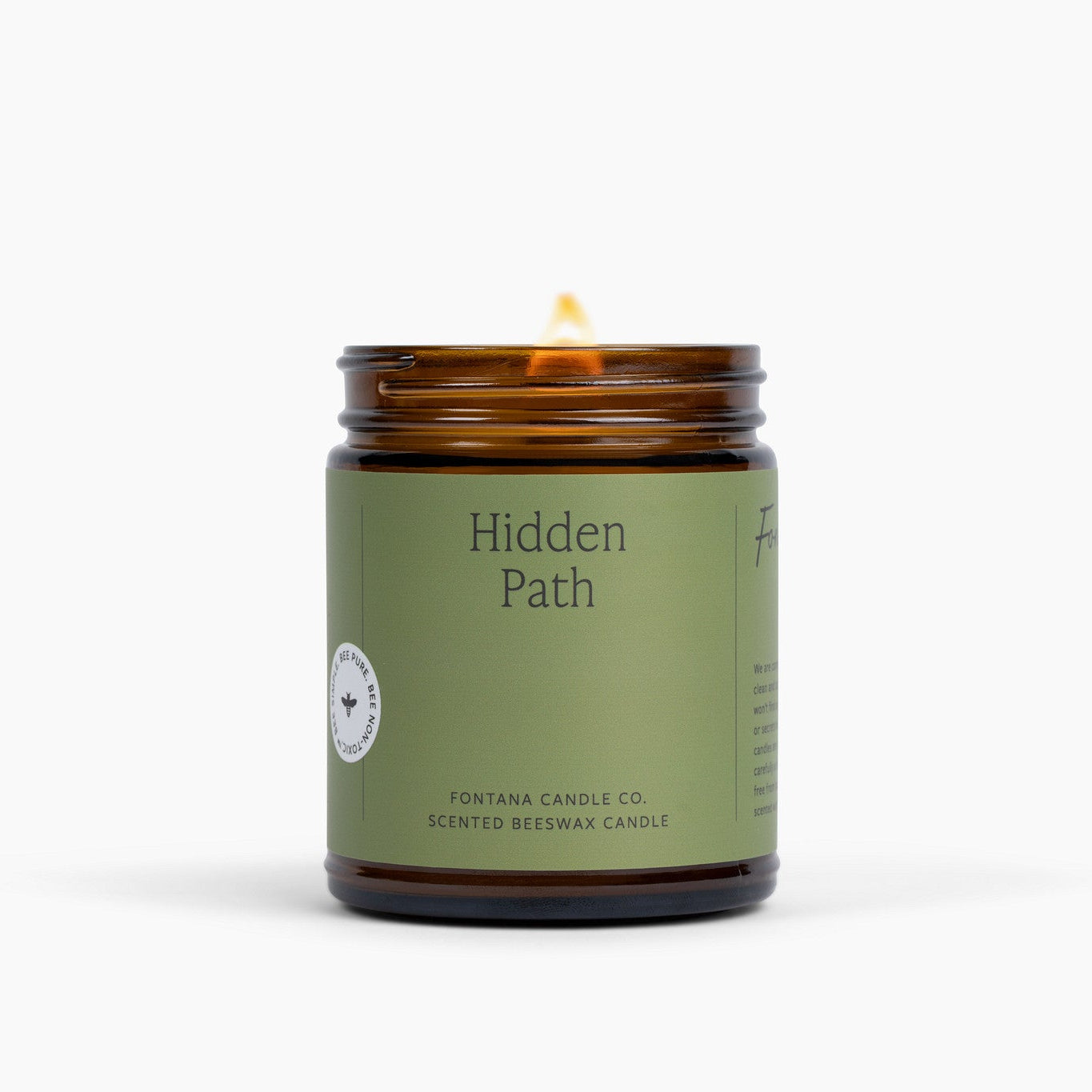 Lit amber glass jar candle with a green label on a white background.