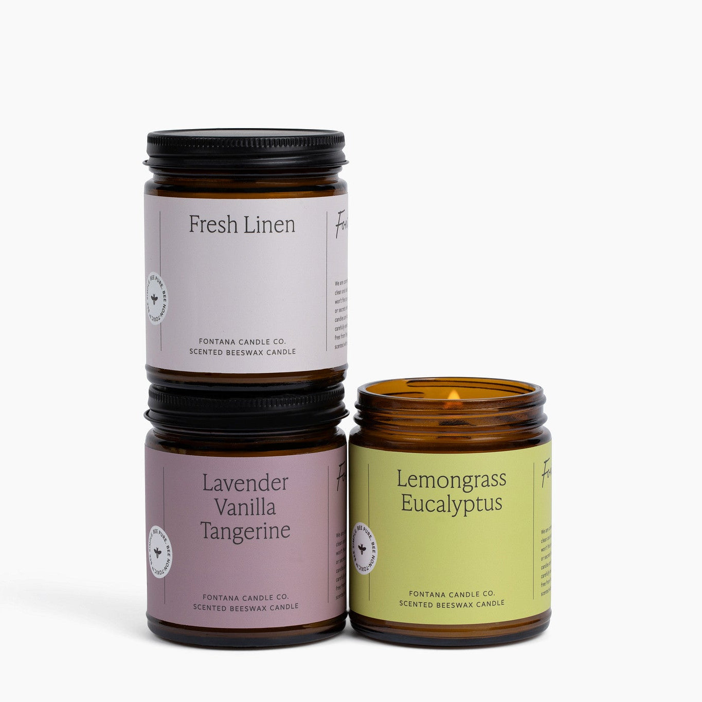 Three amber glass jar candles with colored labels on a white background.