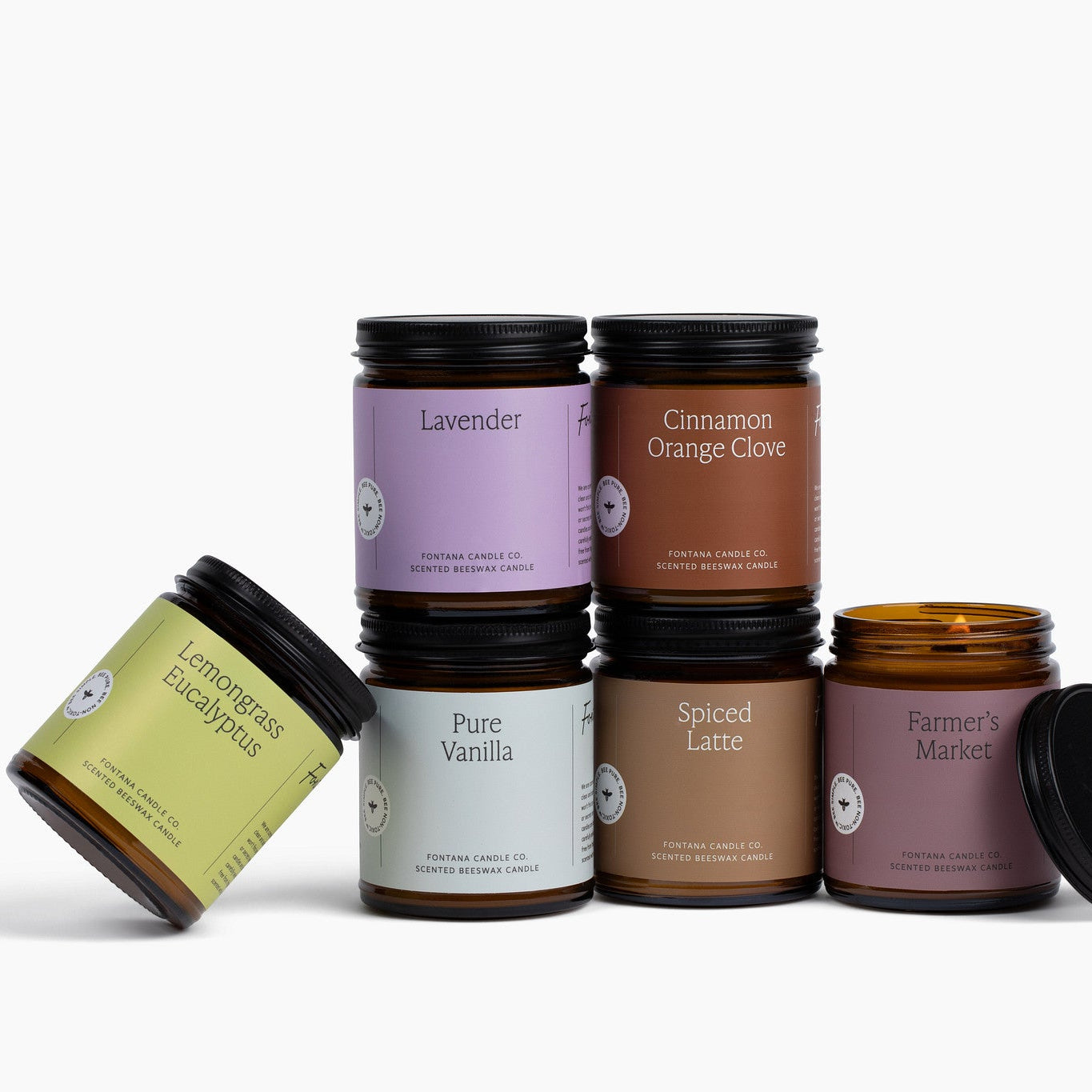 Collection of 6 various scented candles in amber glass jars with colorful labels on a white background