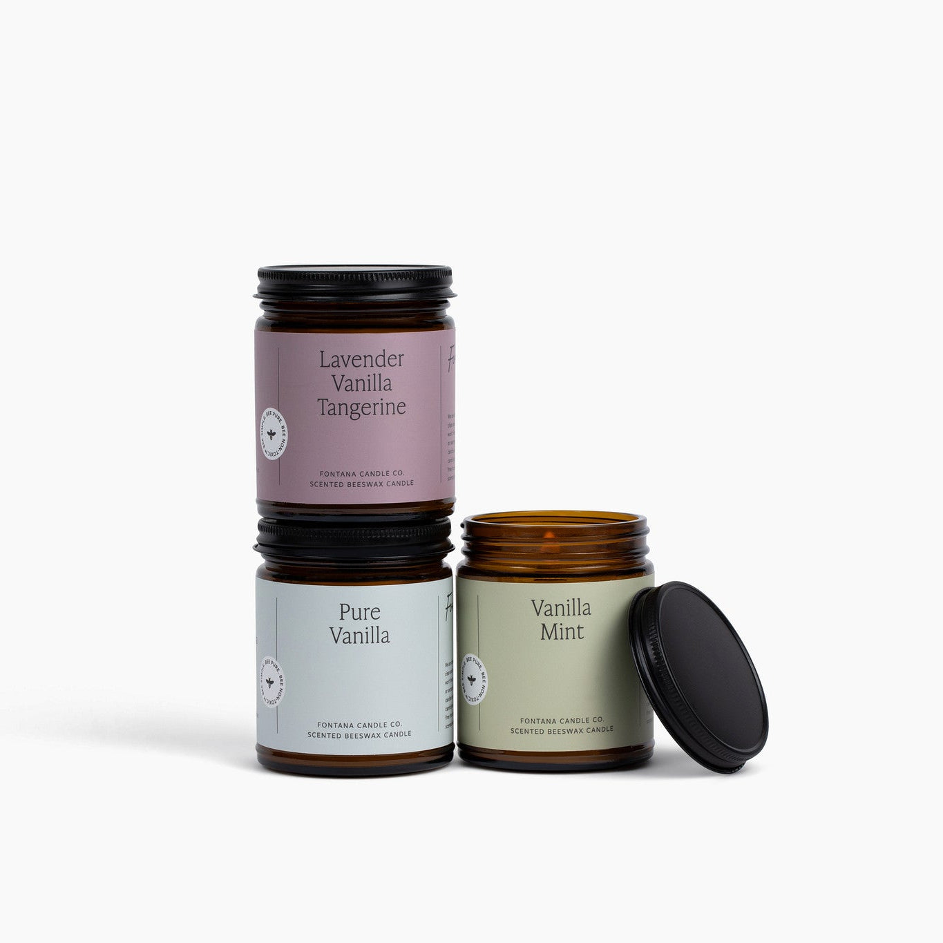 Three amber glass jar candles with different colored labels on a white background.