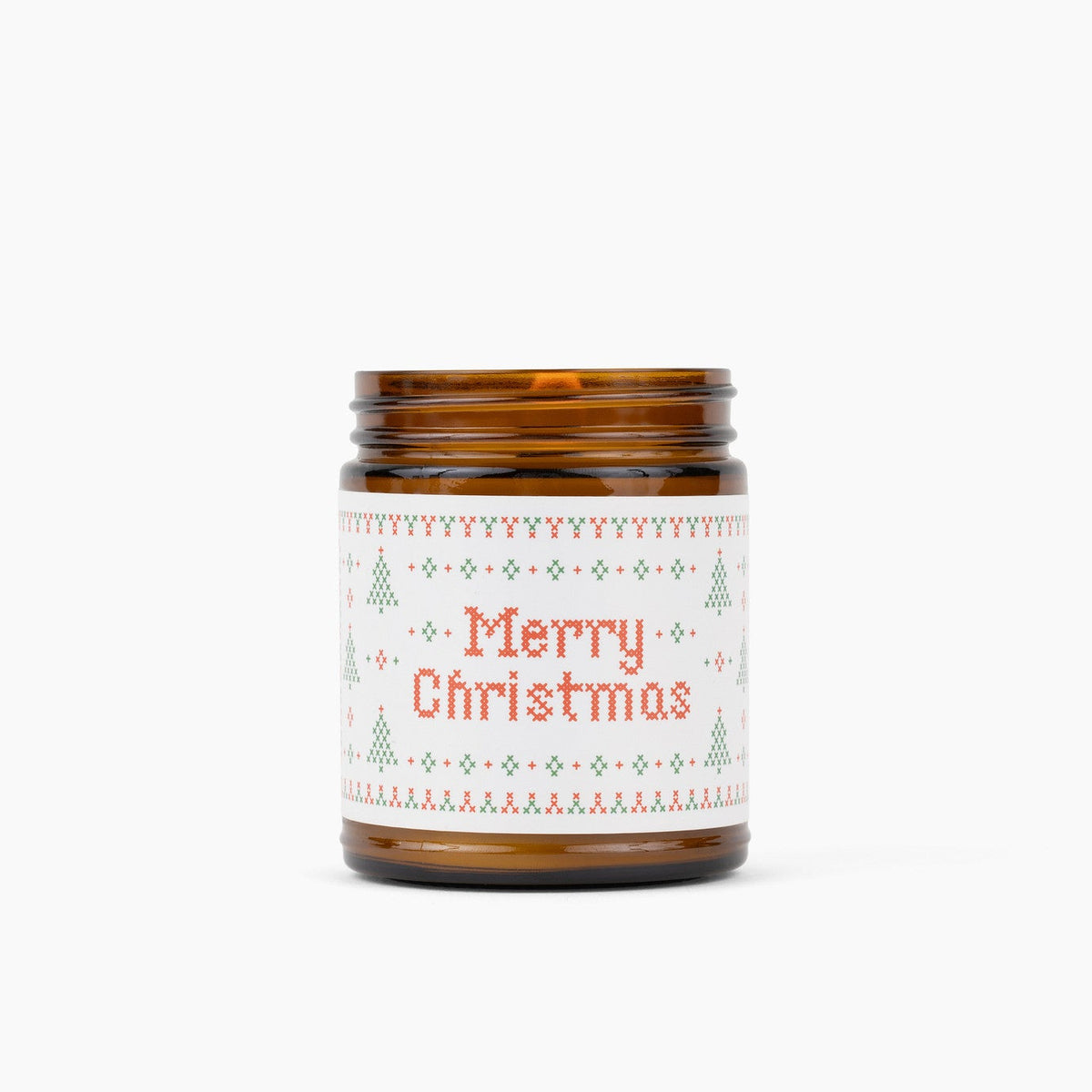 An amber glass jar candle with a white holiday label that reads 'Merry Christmas' in red text, surrounded by a green and red Christmas tree pattern, on a solid white background.