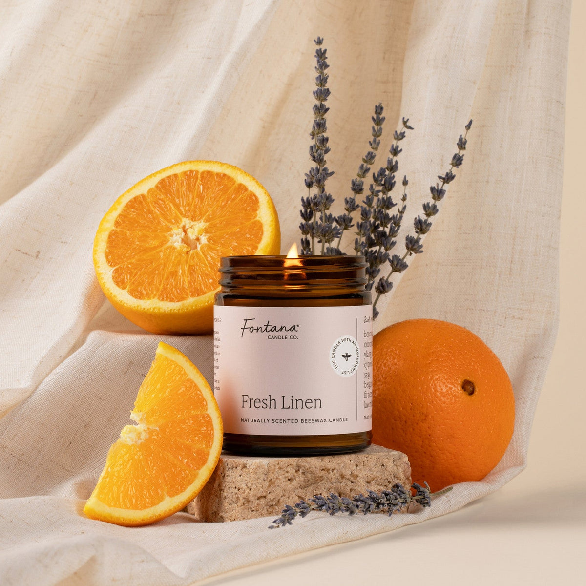 the fresh linen 9oz jar candle posed on a bar of soap with oranges, and lavender buds. 