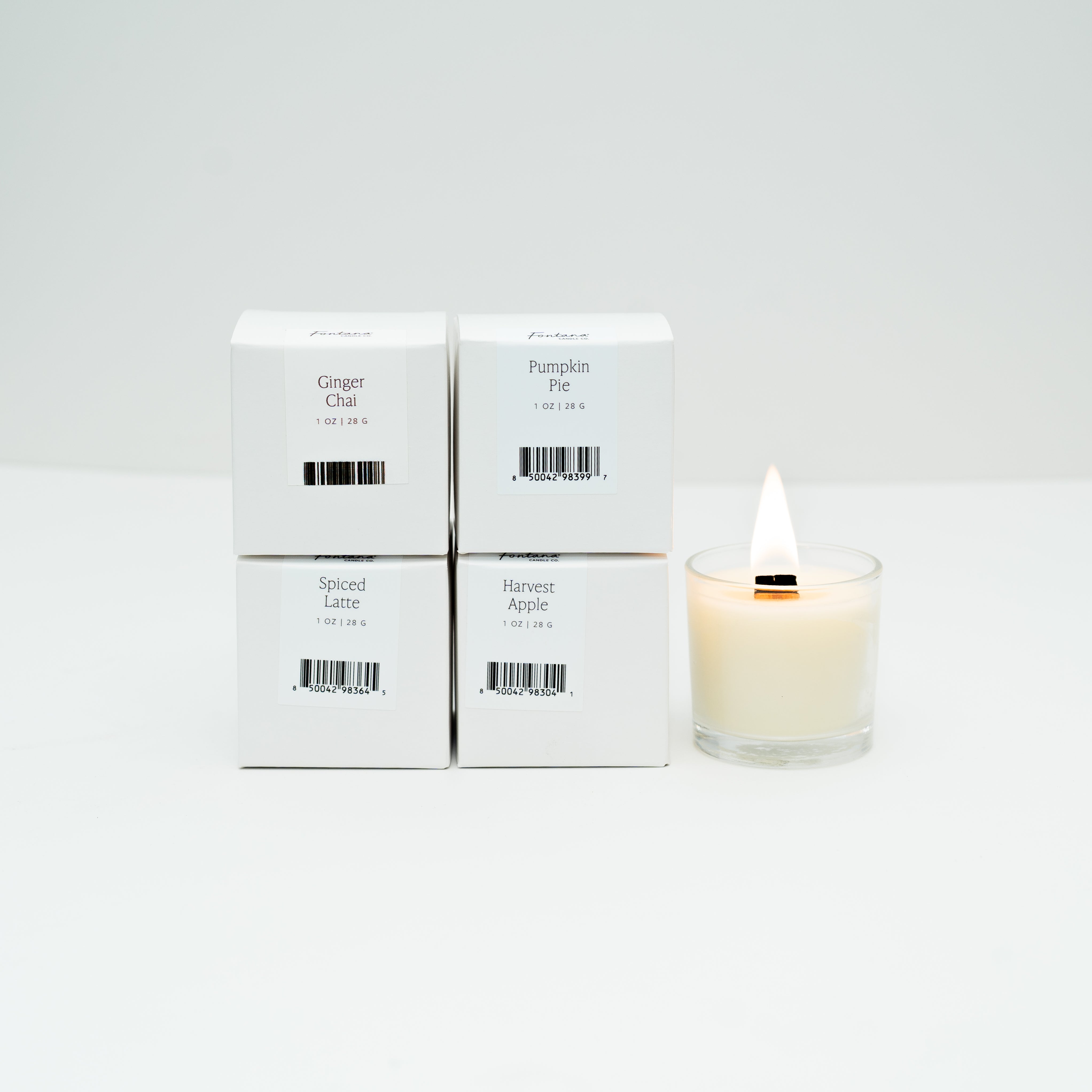 Four boxes of Mini candles next to one lit mini glass votive candle, on a white background.