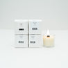 Four boxes of Mini candles next to one lit mini glass votive candle, on a white background.