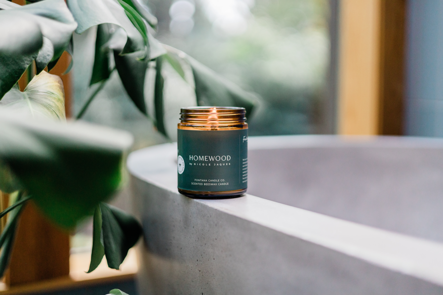 Homewood candle on a ledge of a bathtub with plants in the background