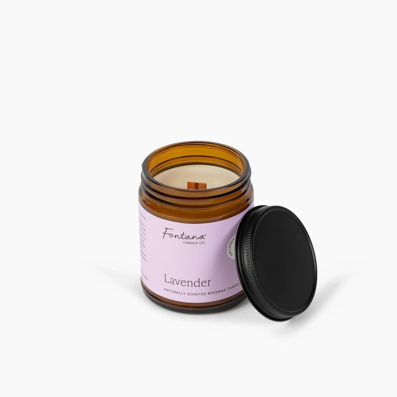 Wooden wick amber glass jar candle with a purple label. The candle is in front of a white background. 