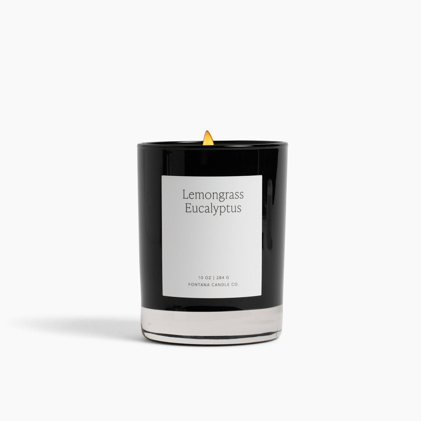 A black glass Noir candle with a white label reading 'Lemongrass Eucalyptus' and a small yellow flame, photographed on a clean white background.