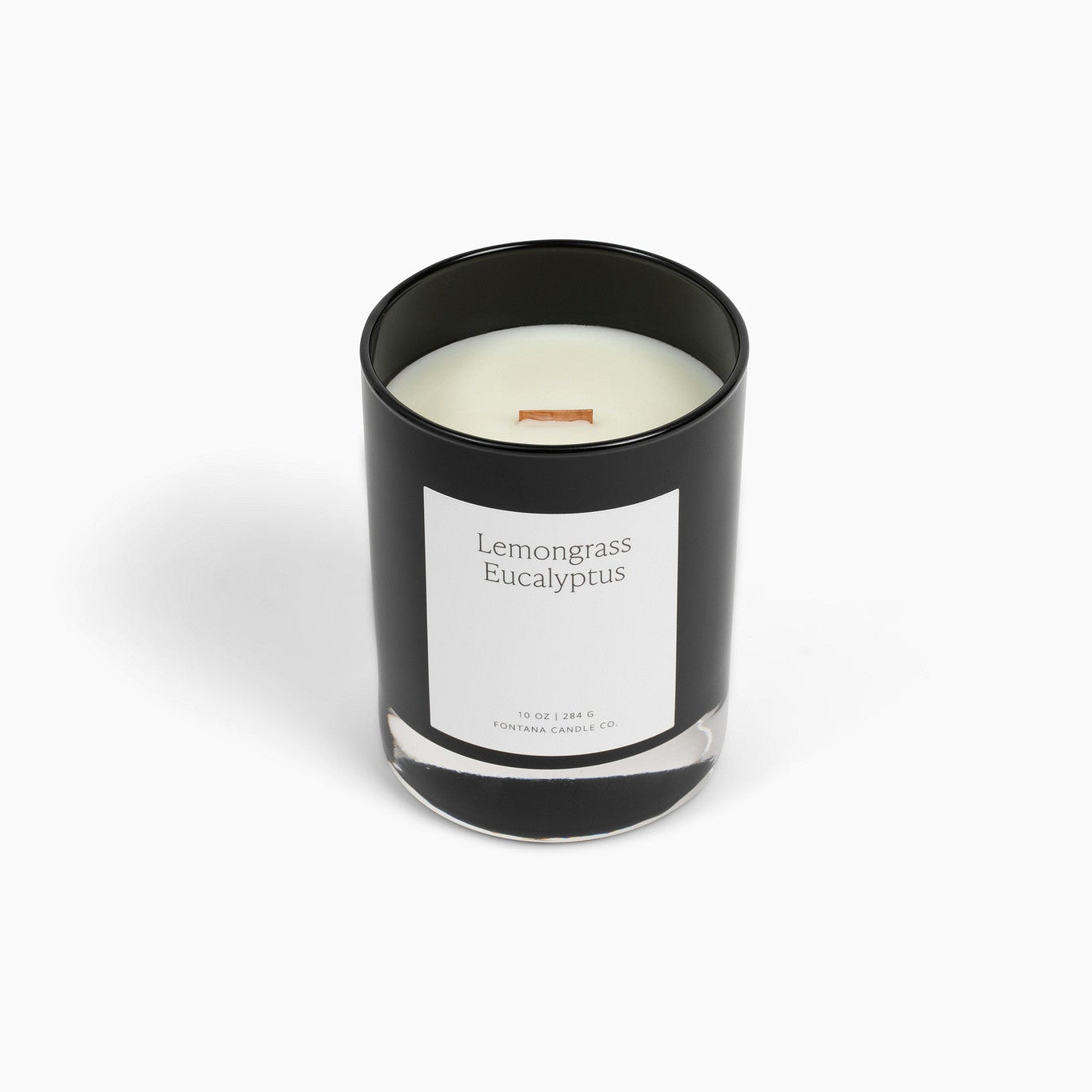 A black glass Noir candle with a white label reading 'Lemongrass Eucalyptus' and a wooden wick, photographed on a clean white 