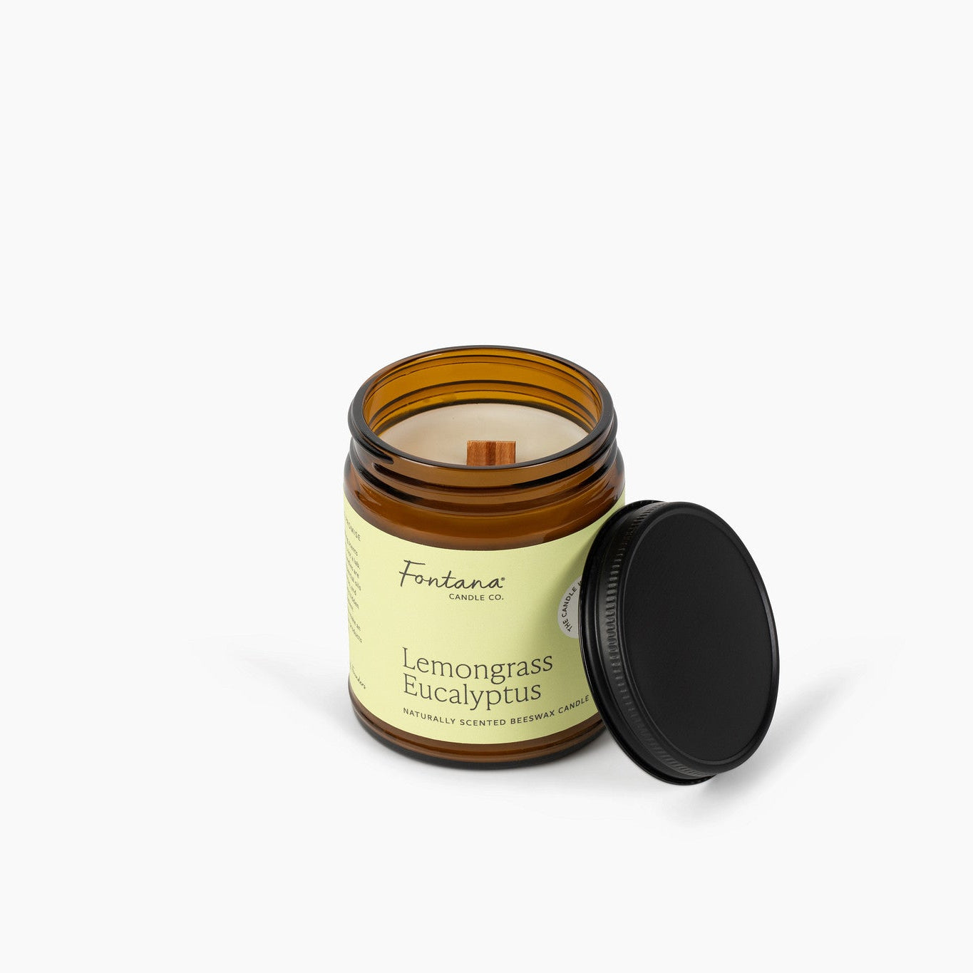 Unlit wooden wick candle in an amber glass jar and a light green label. The candle is in front of a white background. 