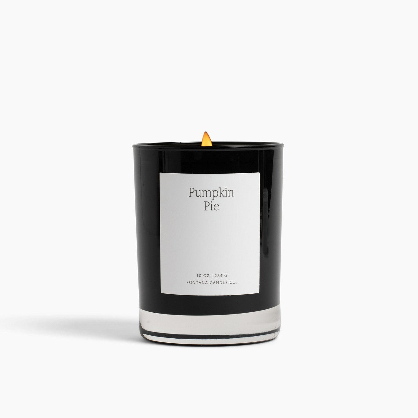 A black glass Noir candle with a white label reading 'Pumpkin Pie' and a small yellow flame, centered on a clean white background.