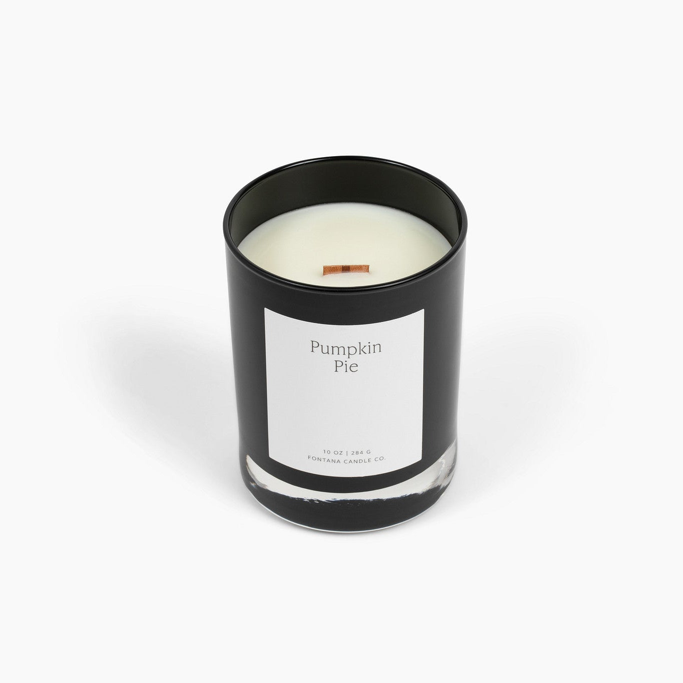 A black glass Noir candle with a white label reading 'Pumpkin Pie' and a small wooden wick, photographed on a clean white background.