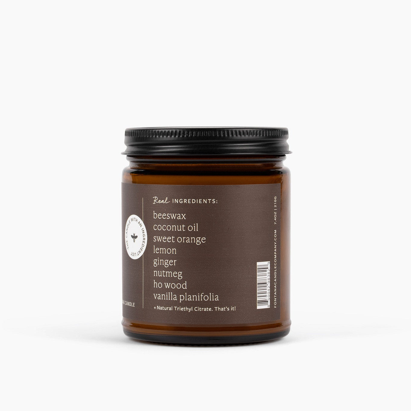 Candle jar with an ingredient label on the side listing beeswax, coconut oil, sweet orange, lemon, ginger, nutmeg, ho wood, vanilla planifolia ingredients on a white background.
