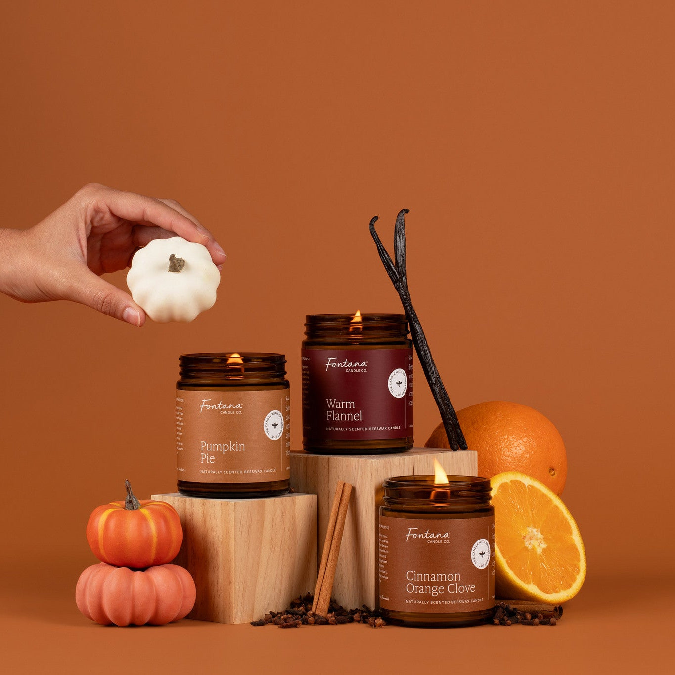Pumpkin Pie, Warm Flannel and Cinnamon Orange Clove Candle surrounded with vanilla beans, pumpkins, oranges, and cinnamon sticks on an orange background