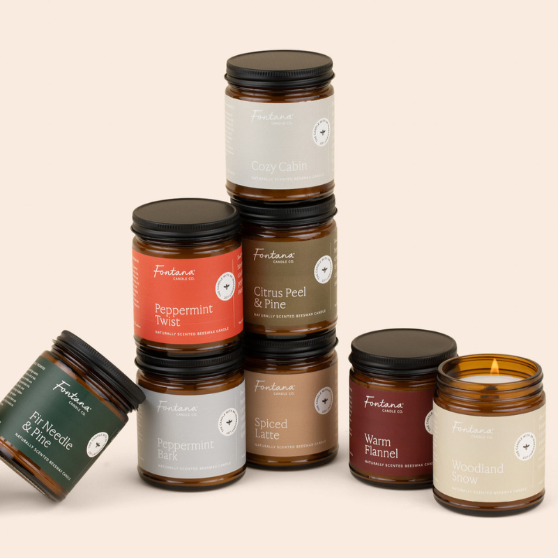 8 holiday amber glass jar candles in front of a cream colored background.