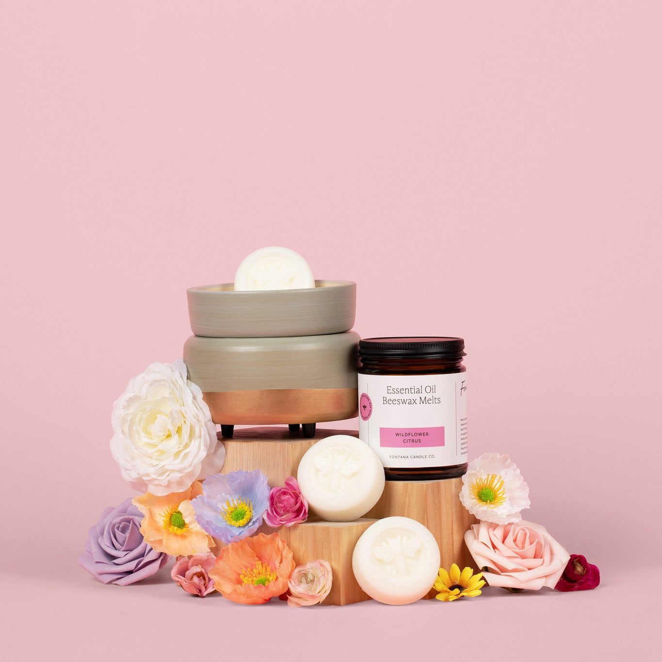 The teal wax melter on a pink background with the wildflower citrus wax melts in it. Surrounded by an assortment of flowers.
