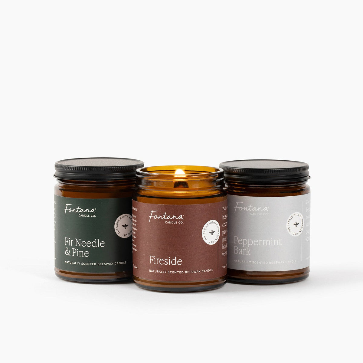 Three candles with labels Fir Needle &amp; Pine, Fireside and Peppermint Bark on a white background