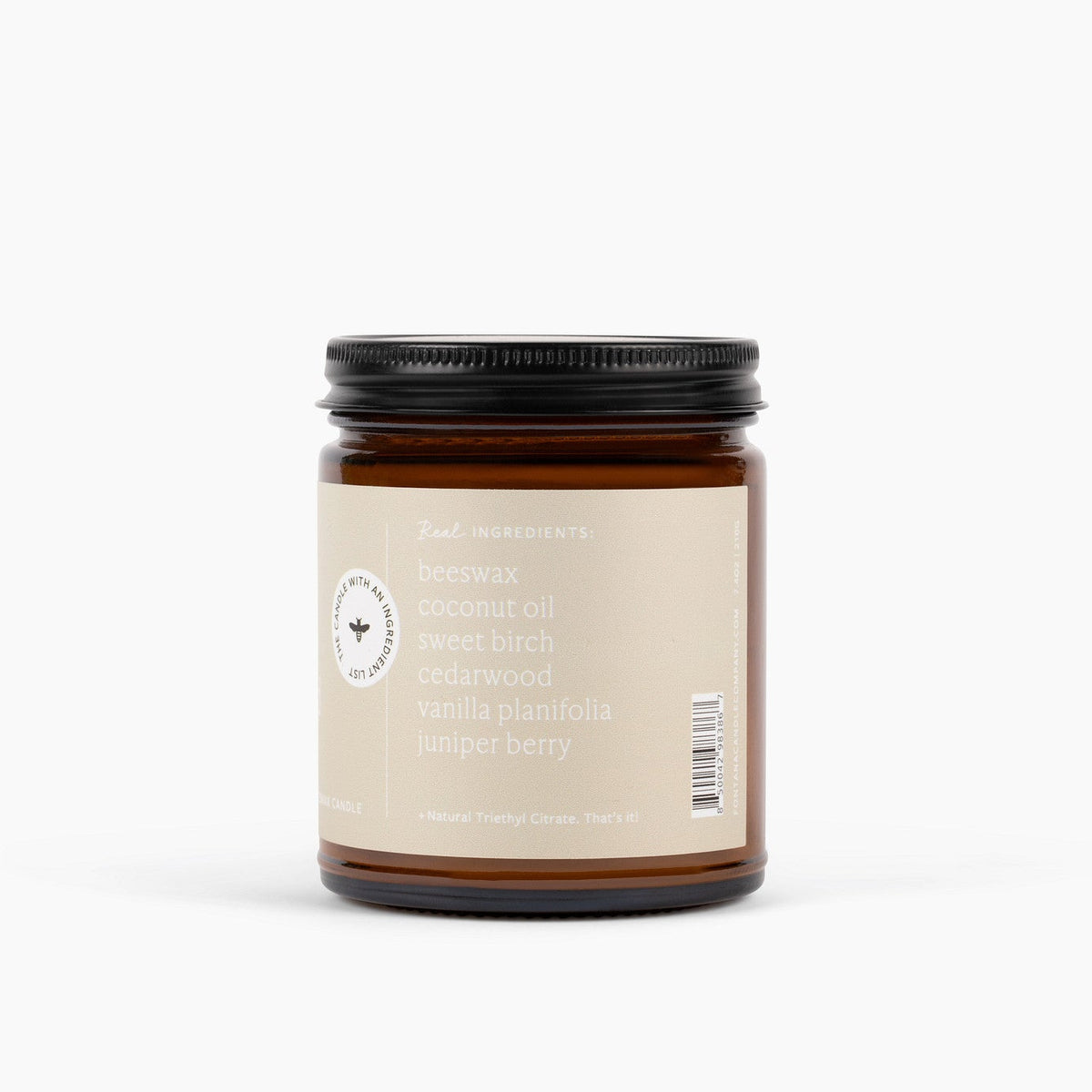 Amber glass jar candle jar with an ingredient label on the side listing beeswax, coconut oil, sweet birch, cedarwood, vanilla planifolia and juniper berry ingredients on a white background