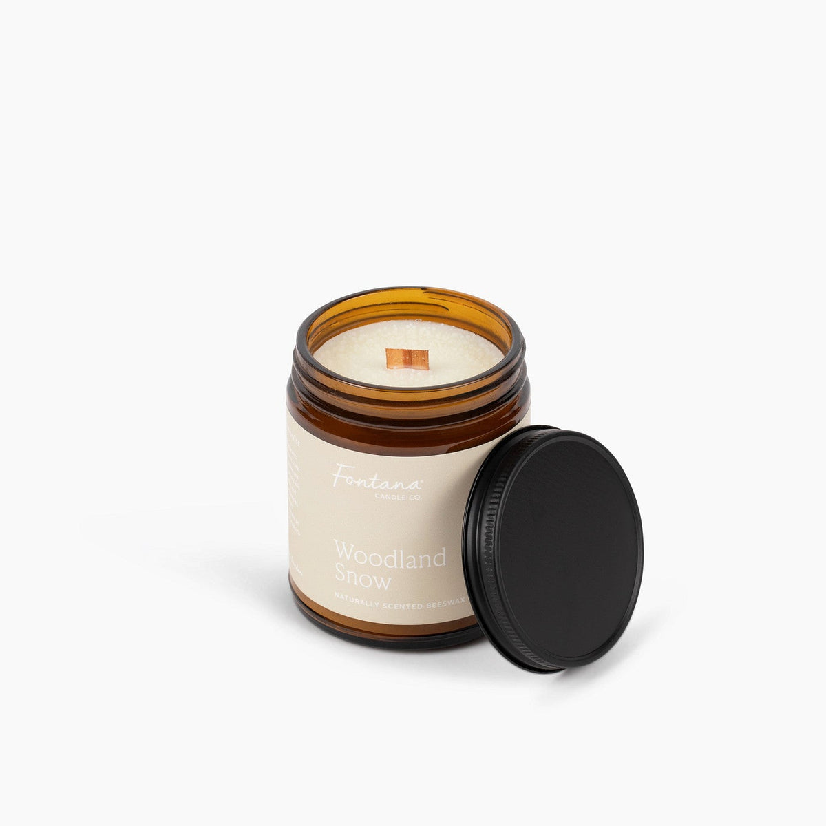Candle in a glass jar with a wooden wick labeled 'Woodland Snow’ on a white background.