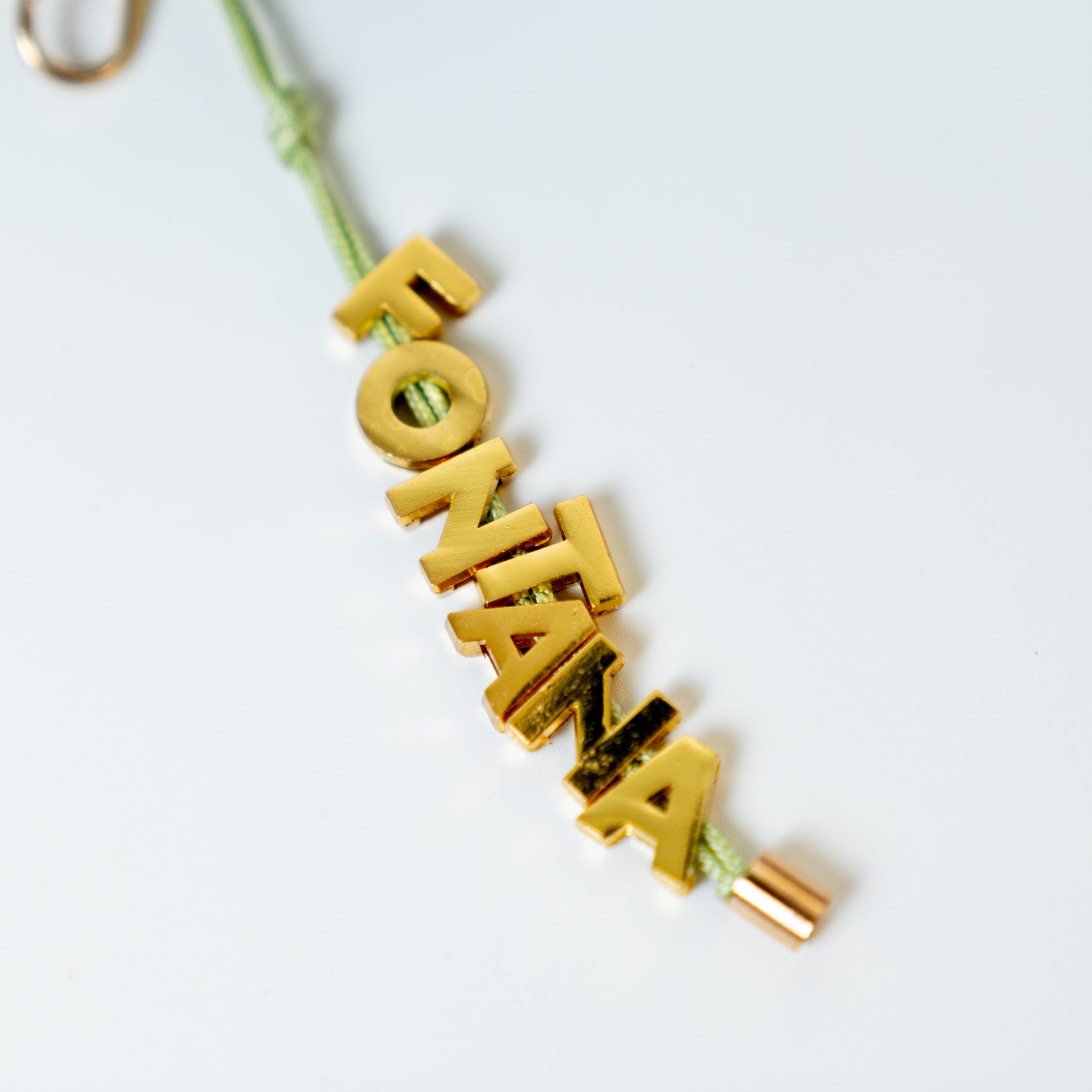 gold Fontana name pendant being held up against a neutral background