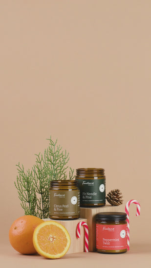 Three candles in glass jars with different scents on a brown background, surrounded by oranges and candy canes.