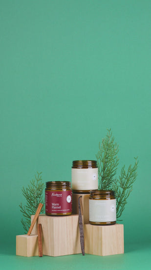 Collection of candles on wooden blocks with greenery against a green background