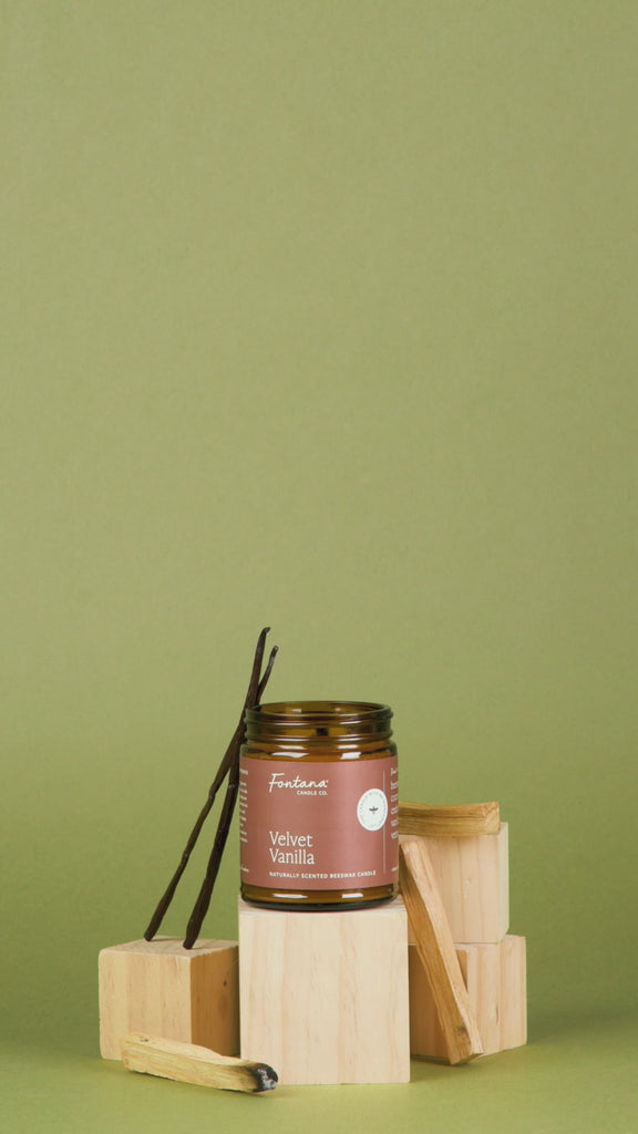 Velvet Vanilla scented candle with vanilla bean on wooden blocks against a green background