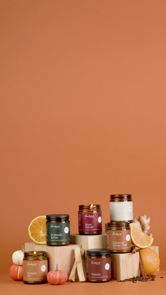 Collection of candles with pumpkins, oranges, and cinnamon sticks on a brown background