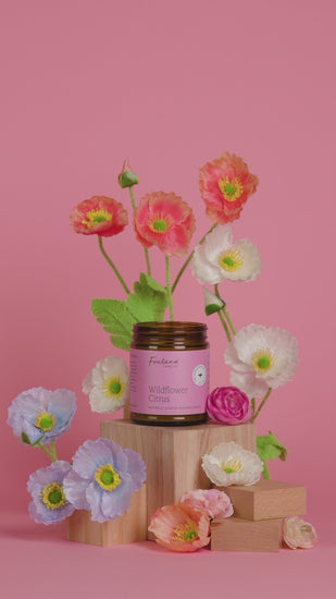 a video of someone lighting the 9oz wildflower citrus jar candle on a pink background