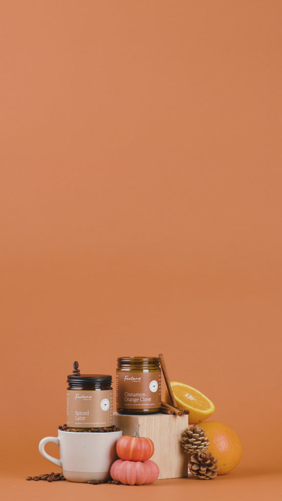 Collection of candles, coffee items, oranges and pinecones on an orange background