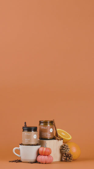 Collection of candles, coffee items, oranges and pinecones on an orange background