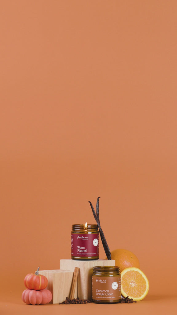 Pumpkin Pie, Warm Flannel and Cinnamon Orange Clove Candle surrounded with vanilla beans, pumpkins, oranges, and cinnamon sticks on an orange background